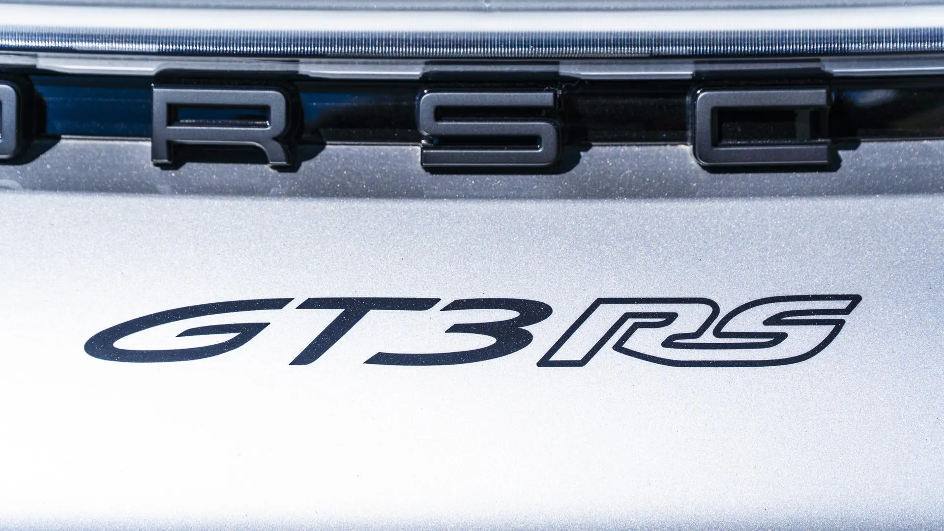 Close-up of the Porsche GT3 RS badge on the rear of a silver sports car.