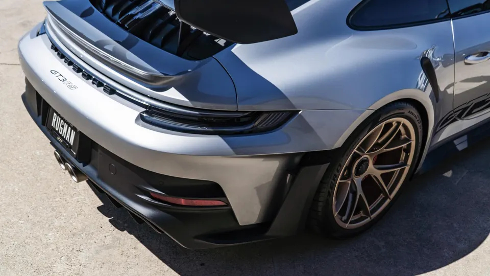 Silver Porsche GT3 RS rear quarter view showcasing bronze wheels, aggressive diffuser, and dual exhaust tips.