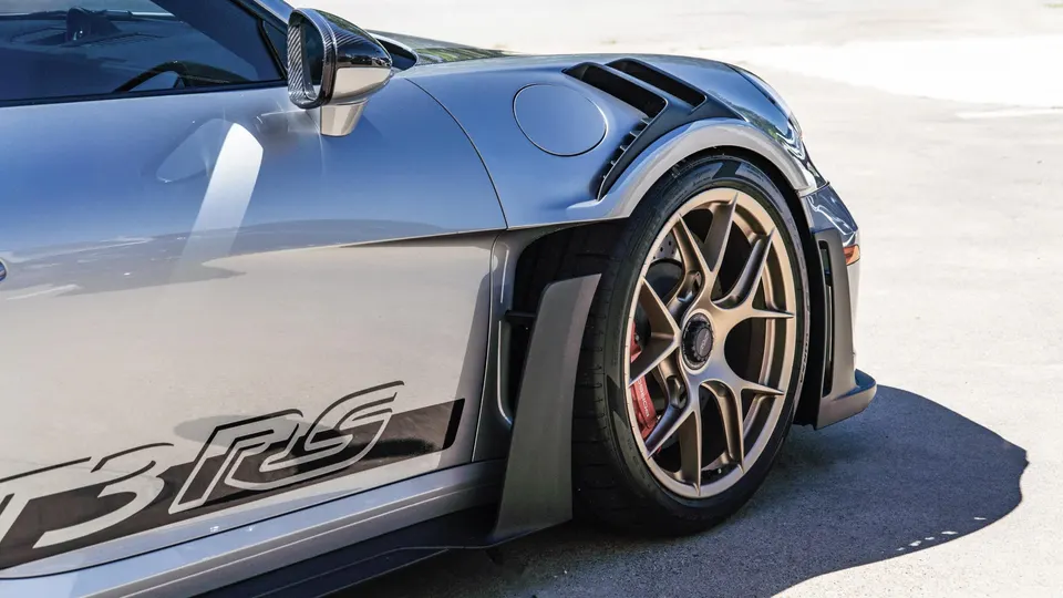A close-up of a silver Porsche GT3RS showing its custom bronze wheels, red brake calipers, and widebody fender.
