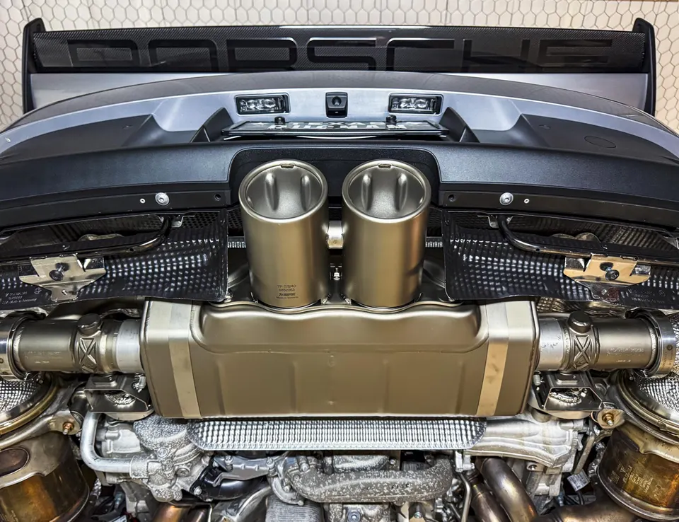 Close-up view of a Porsche's Akrapovic exhaust system with dual tips and a carbon fiber rear wing.