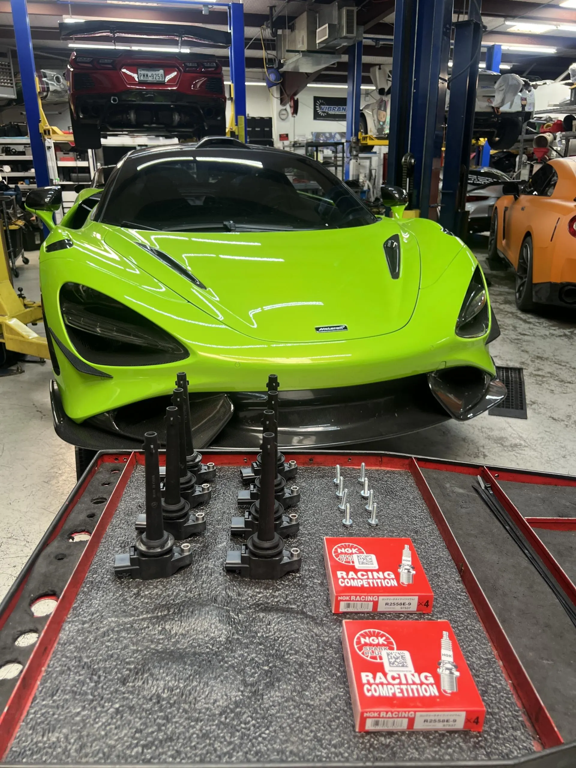 A bright green McLaren 720S in a performance shop with new ignition coils and NGK spark plugs on a workbench.