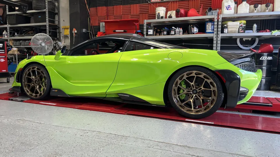 Lime green McLaren 720S with custom bronze wheels on red platforms in a performance tuning shop.