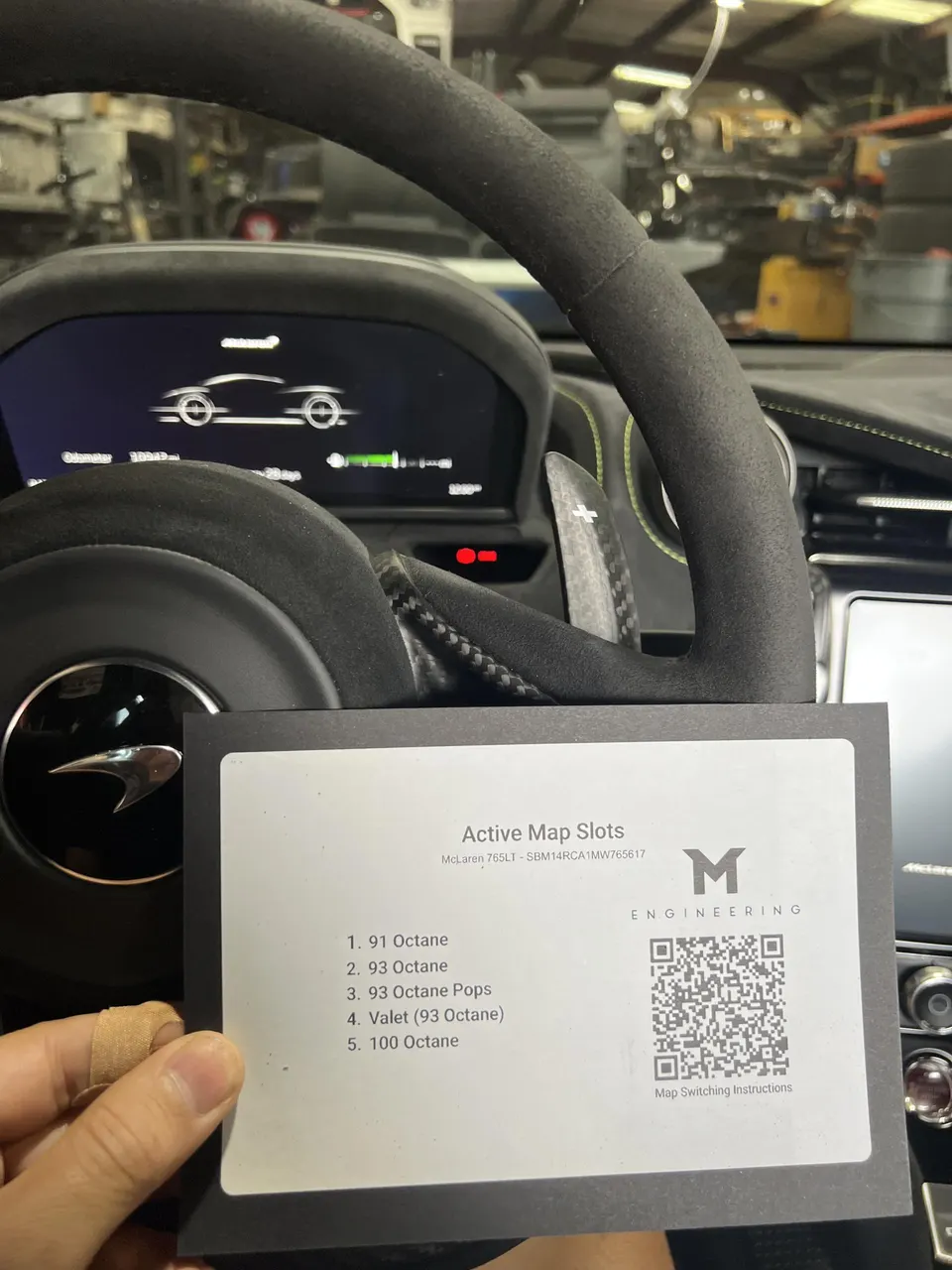 Hand holding a card with active ECU map slots for a McLaren 765LT, detailing 91, 93, and 100 octane tunes in a shop.