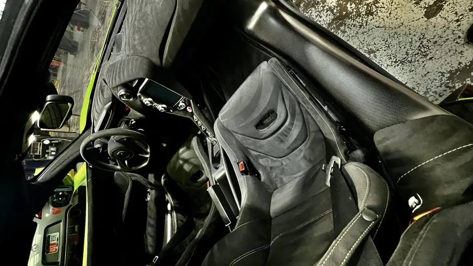 Interior view of a McLaren supercar, featuring black Alcantara sports seats, carbon fiber trim, and a minimalist dashboard.