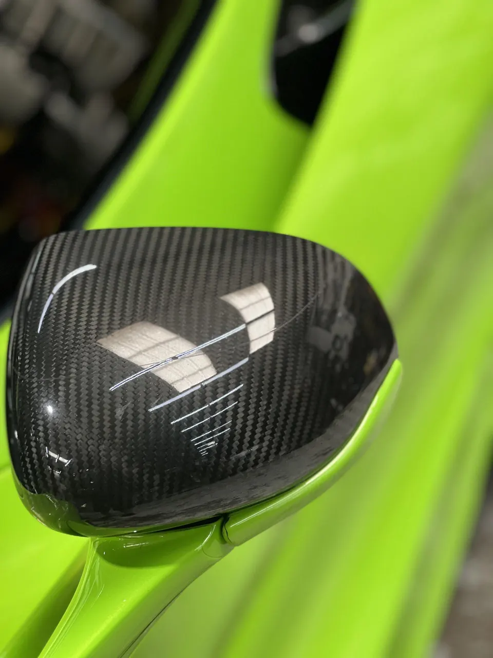 Close-up of a carbon fiber side mirror on a bright green performance car, showcasing the weave and finish.