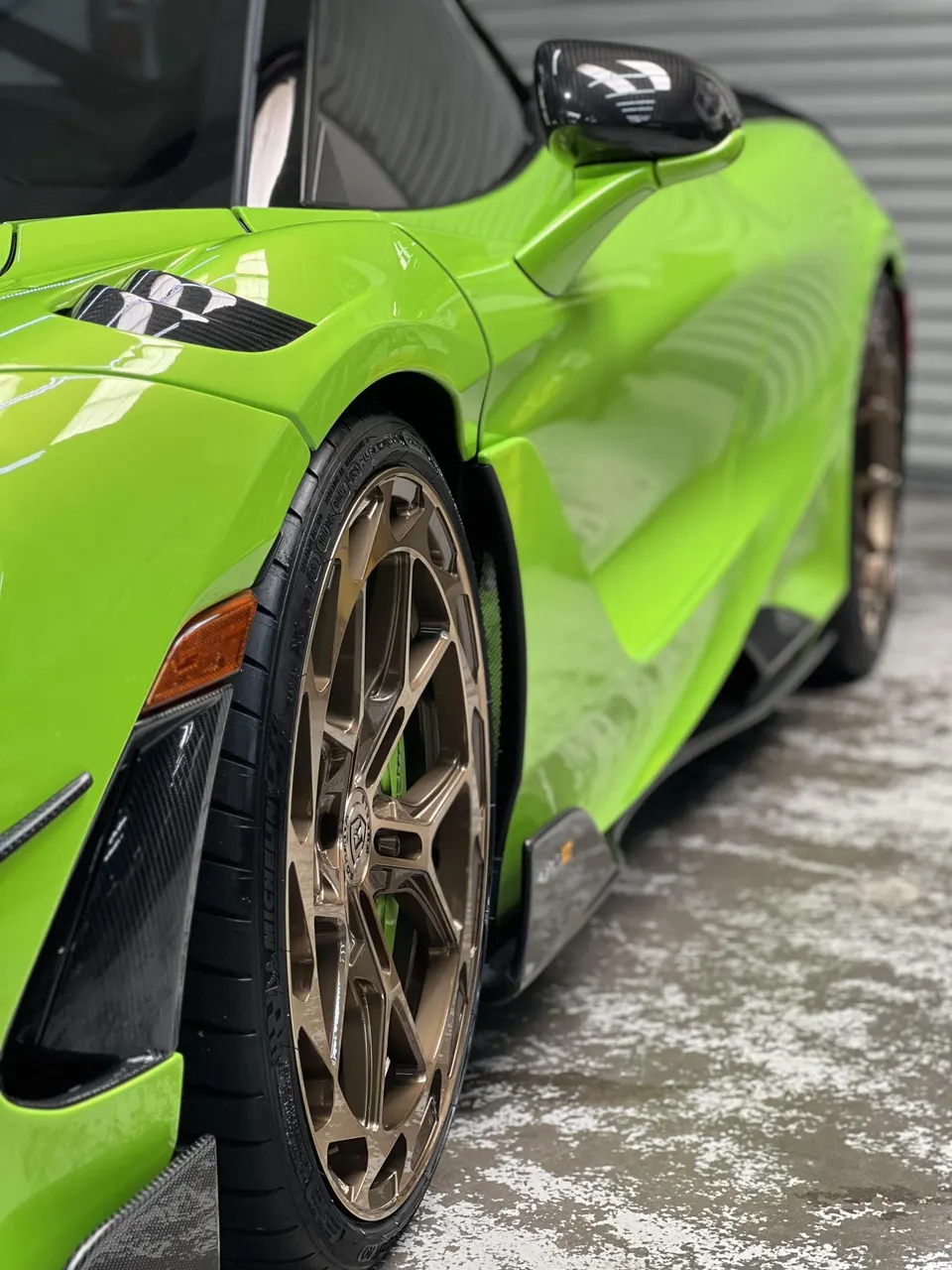 Lime green McLaren supercar with custom bronze wheels and carbon fiber accents parked in a garage.