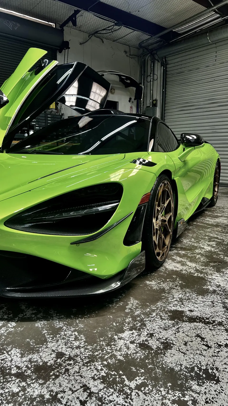 A vibrant green McLaren 720S with custom bronze wheels and carbon fiber aero parked in a garage with its doors open.