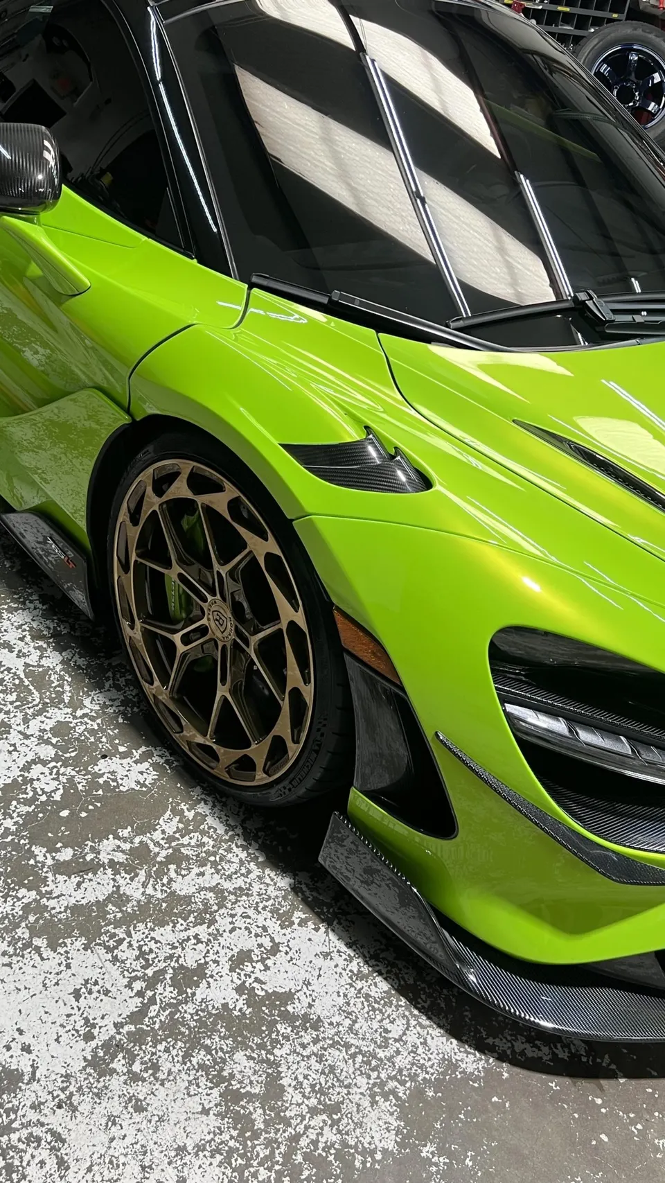 Close-up of a lime green McLaren with custom bronze wheels and carbon fiber aerodynamic elements.