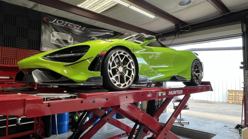 A vibrant lime green McLaren 720S supercar sits elevated on a red car lift inside a performance tuning shop.