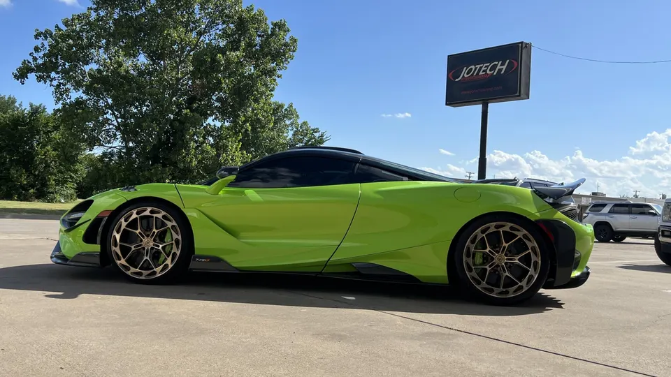 A lime green McLaren 720S with aftermarket wheels parked outside Jotech Motorsports under a blue sky.