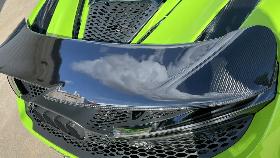 A close-up of a lime green McLaren's rear, showcasing a carbon fiber wing and quad exhaust tips.