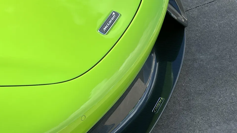 A close-up of a bright green McLaren's front bumper and carbon fiber Jotech splitter.