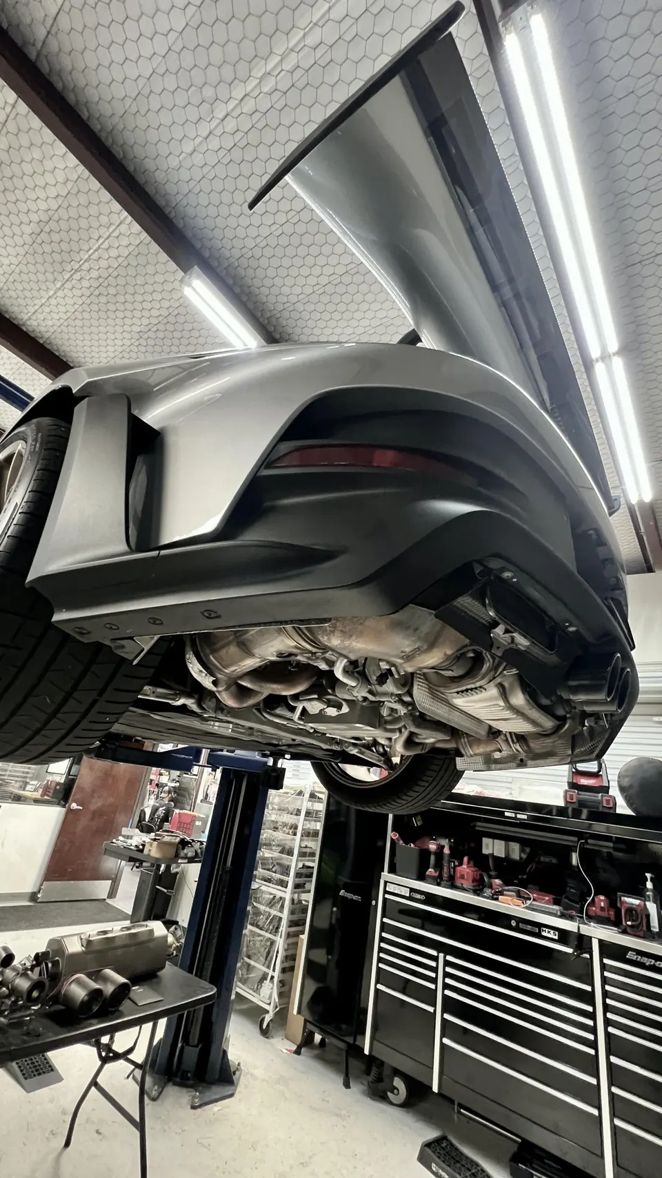 A Porsche 911 on a lift in a performance shop, showcasing the underbody and exhaust system during an upgrade.