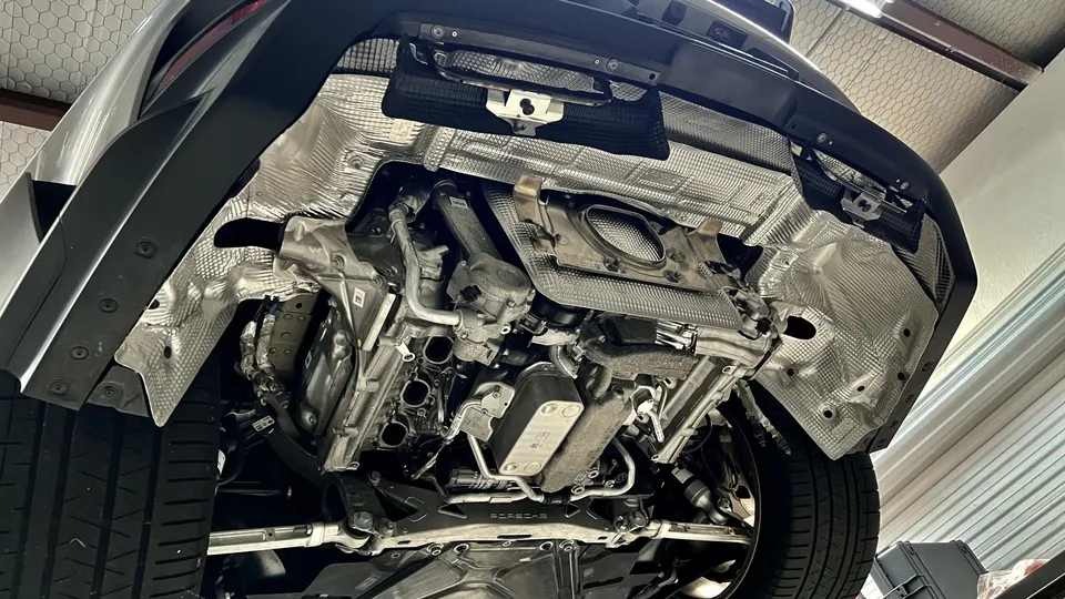 Underside view of a car on a lift, showcasing the exhaust system, heat shields, and suspension components.