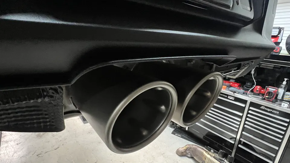 Close-up of black aftermarket exhaust tips on a performance car in a shop setting