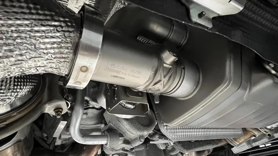 A close-up view of an Akrapovic exhaust system installed on the underside of a performance car, showing the muffler and heat shielding.