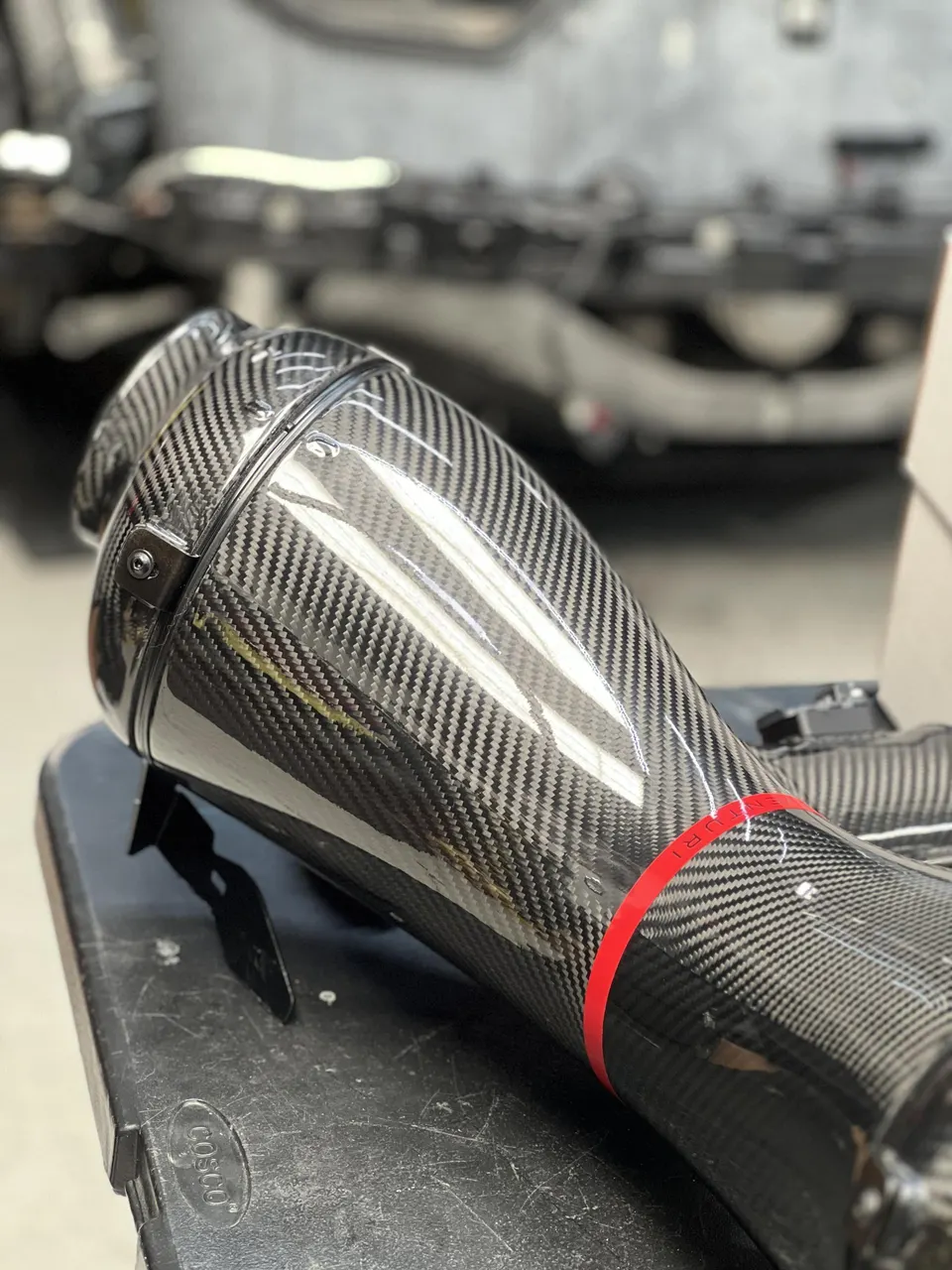 Close-up of a carbon fiber intake system with a red Venturi ring, likely for a high-performance car.