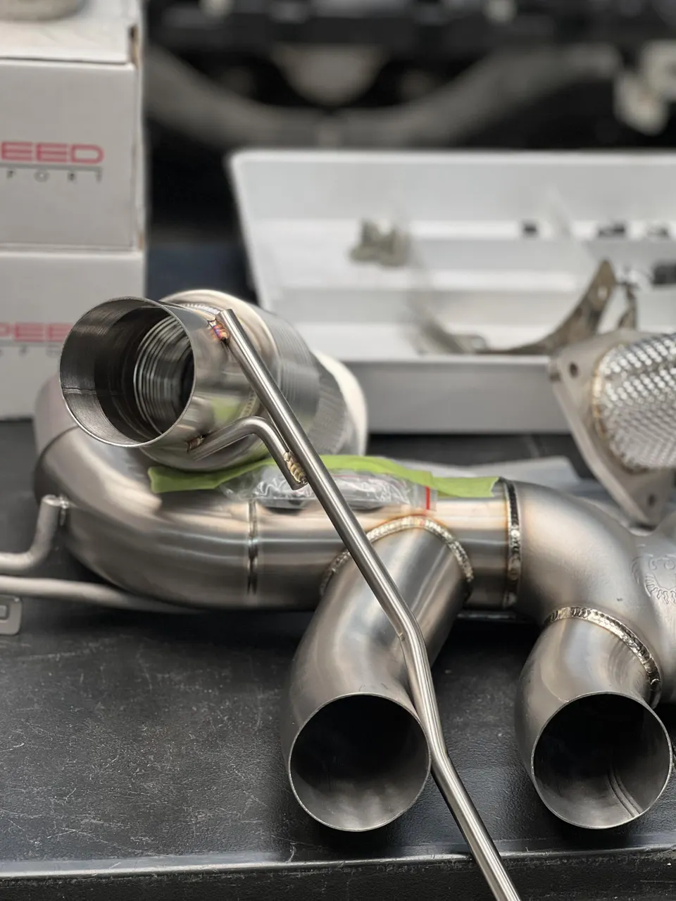Close-up of a new titanium exhaust system with visible welds, ready for installation in a performance shop.