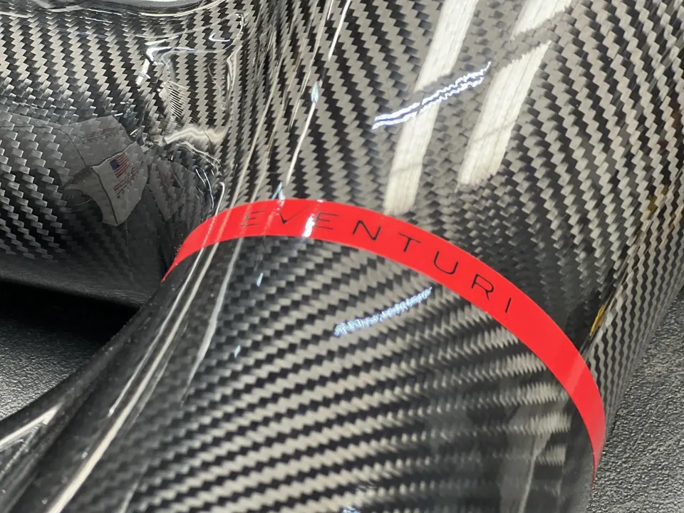 Close-up of a carbon fiber Venturi intake system component with a red band, showcasing the weave.