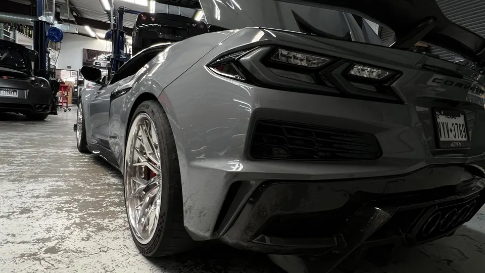 A grey Chevrolet Corvette C8 with custom chrome wheels parked in a Jotech Motorsports shop.