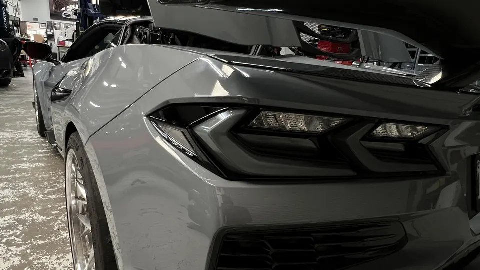 A grey Corvette C8 with its engine bay open, parked in a performance tuning shop.