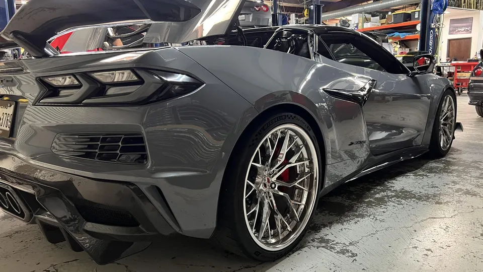 Grey Chevrolet Corvette C8 with aftermarket chrome wheels and red brake calipers in a performance shop.