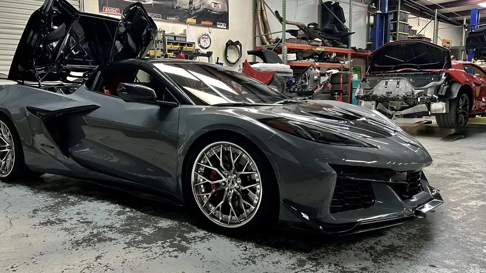 A grey Corvette Z06 with custom wheels and its engine bay open, parked in a performance tuning shop.