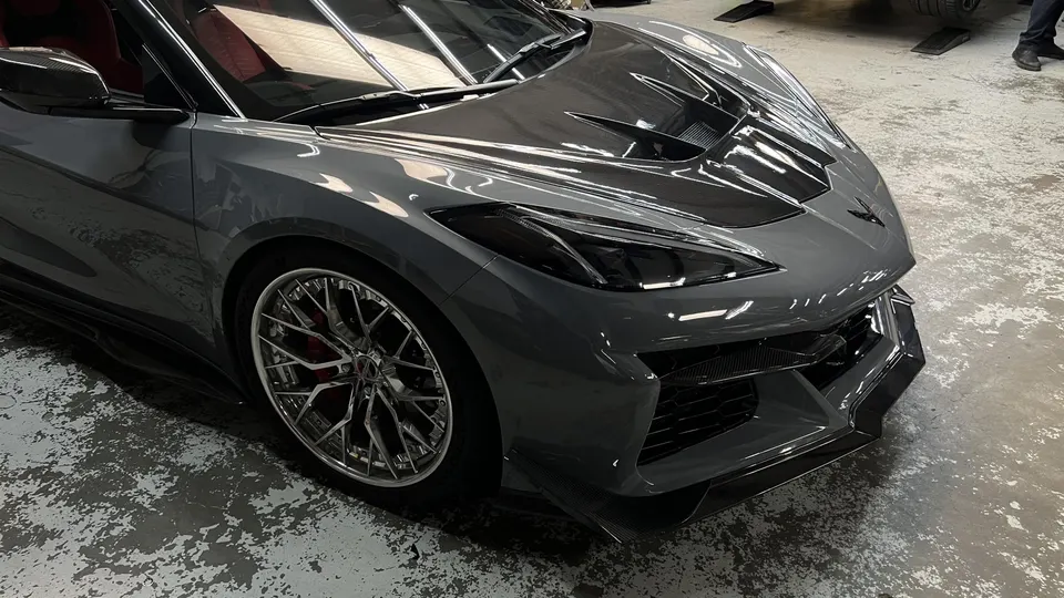 A grey Chevrolet Corvette C8 with custom chrome wheels and carbon fiber aerodynamic parts in a garage.