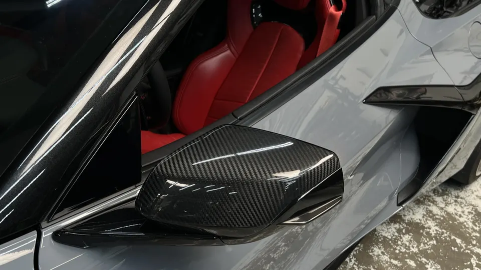Close-up of a grey Corvette C8 with a carbon fiber side mirror and red interior.