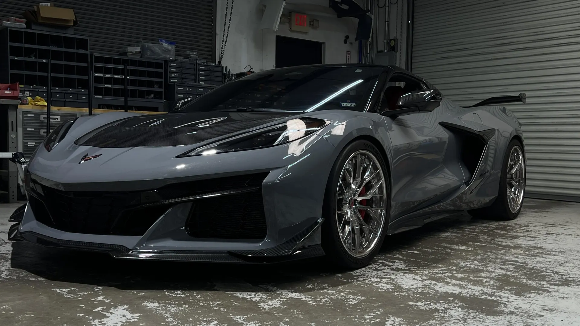 Grey Chevrolet Corvette Z06 with carbon fiber hood, front splitter, side skirts, and rear wing in a shop.