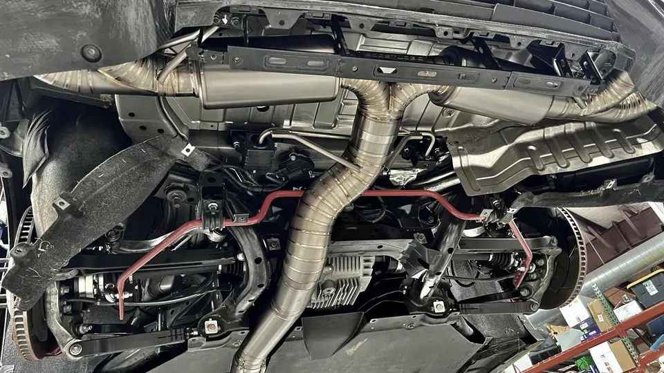 Underside view of a performance car showing a custom titanium exhaust system and red aftermarket sway bars.