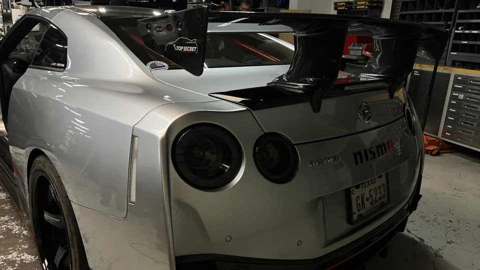 A silver Nissan GT-R R35 with a large carbon fiber wing and Nismo badging in a shop environment.