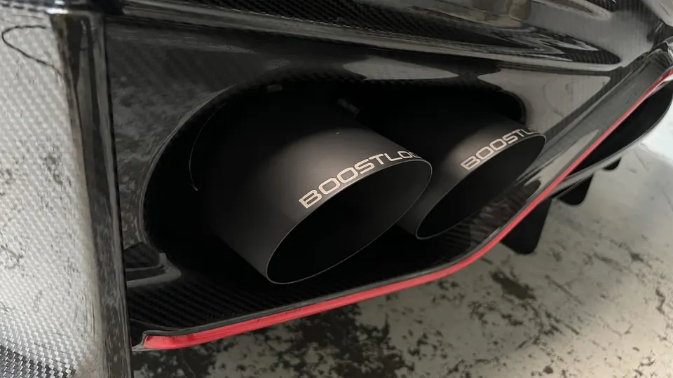 Close-up of Boost Logic exhaust tips integrated into a carbon fiber rear diffuser with red trim.