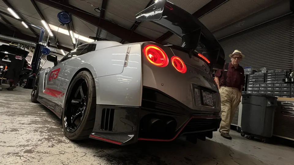 A silver Nissan GT-R with a large carbon fiber wing and diffuser parked in a performance tuning shop.