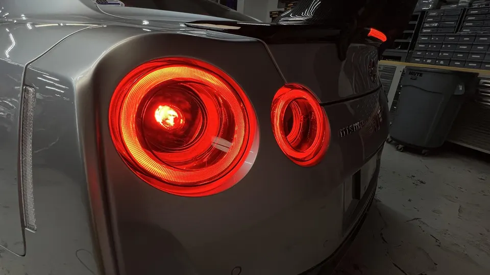 Close-up of the illuminated red taillights and Nismo spoiler on a silver Nissan GT-R R35 in a shop environment.