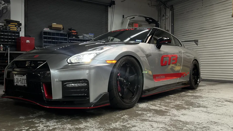 Silver Nissan GT-R R35 with carbon fiber hood, aftermarket wheels, and GT3 livery parked in a performance shop.