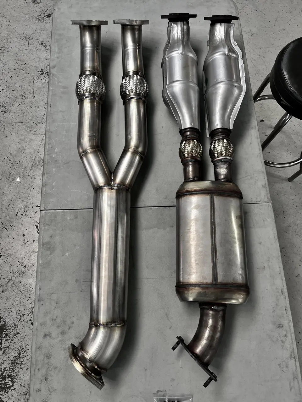 Stainless steel exhaust downpipes and catalytic converter assembly laid out in a shop.