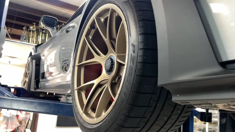 A silver Porsche 911 GT3 RS on a car lift in a shop, showcasing its gold multi-spoke wheels and Pirelli P Zero tires.