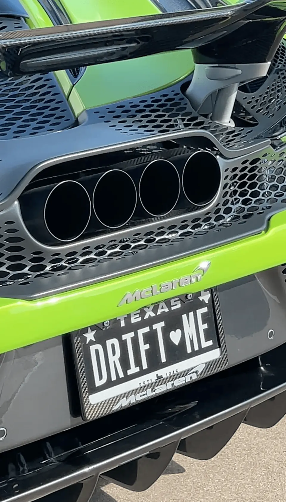 A close-up of the rear of a lime green McLaren, showcasing its quad exhaust tips, carbon fiber diffuser, and a custom Texas license plate.