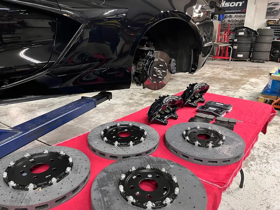 A black Corvette on a lift in a shop with new performance brake rotors and calipers laid out for installation.
