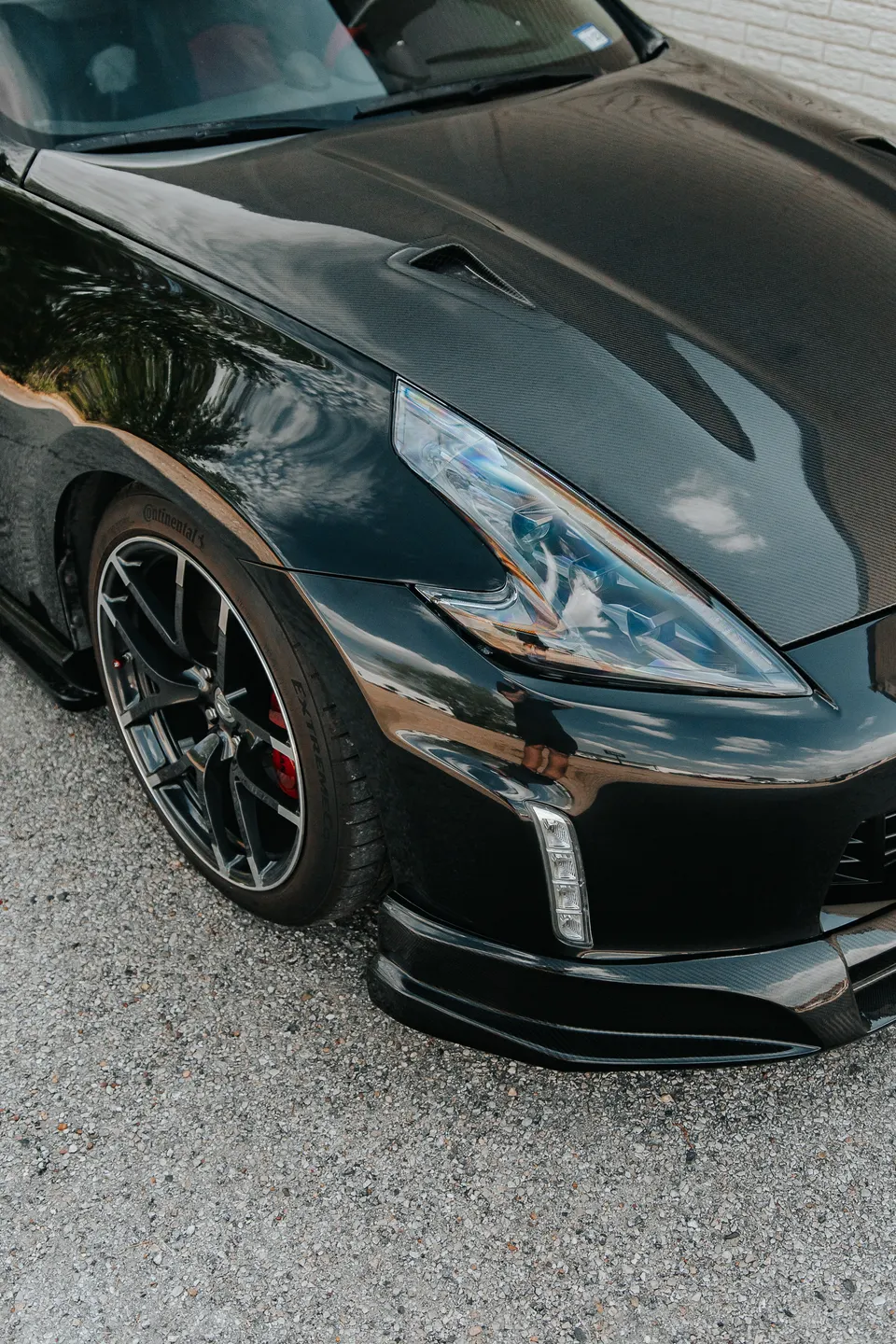Close-up of a black Nissan 370Z featuring a carbon fiber hood, aftermarket wheels, and a front splitter.