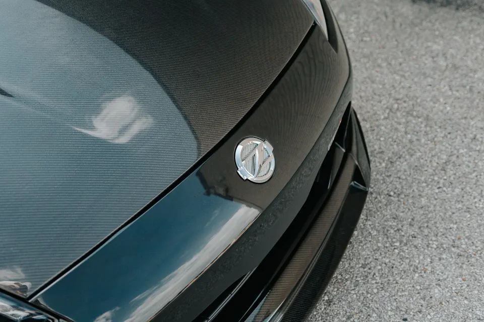 A close-up of a car's carbon fiber hood and front bumper with a custom emblem.