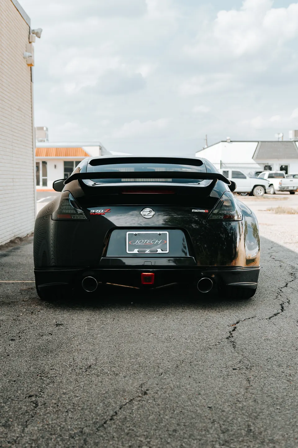 Rear view of a black Nissan 370Z with a spoiler and dual exhaust, parked outdoors next to a building.