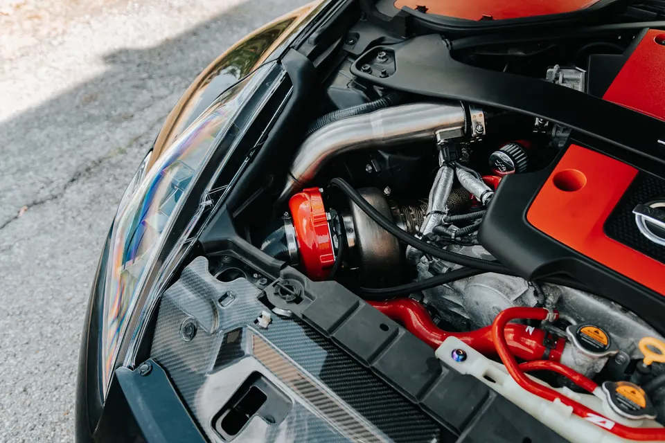 A close-up view of a Nissan engine bay featuring a prominent red turbocharger and custom boost piping.