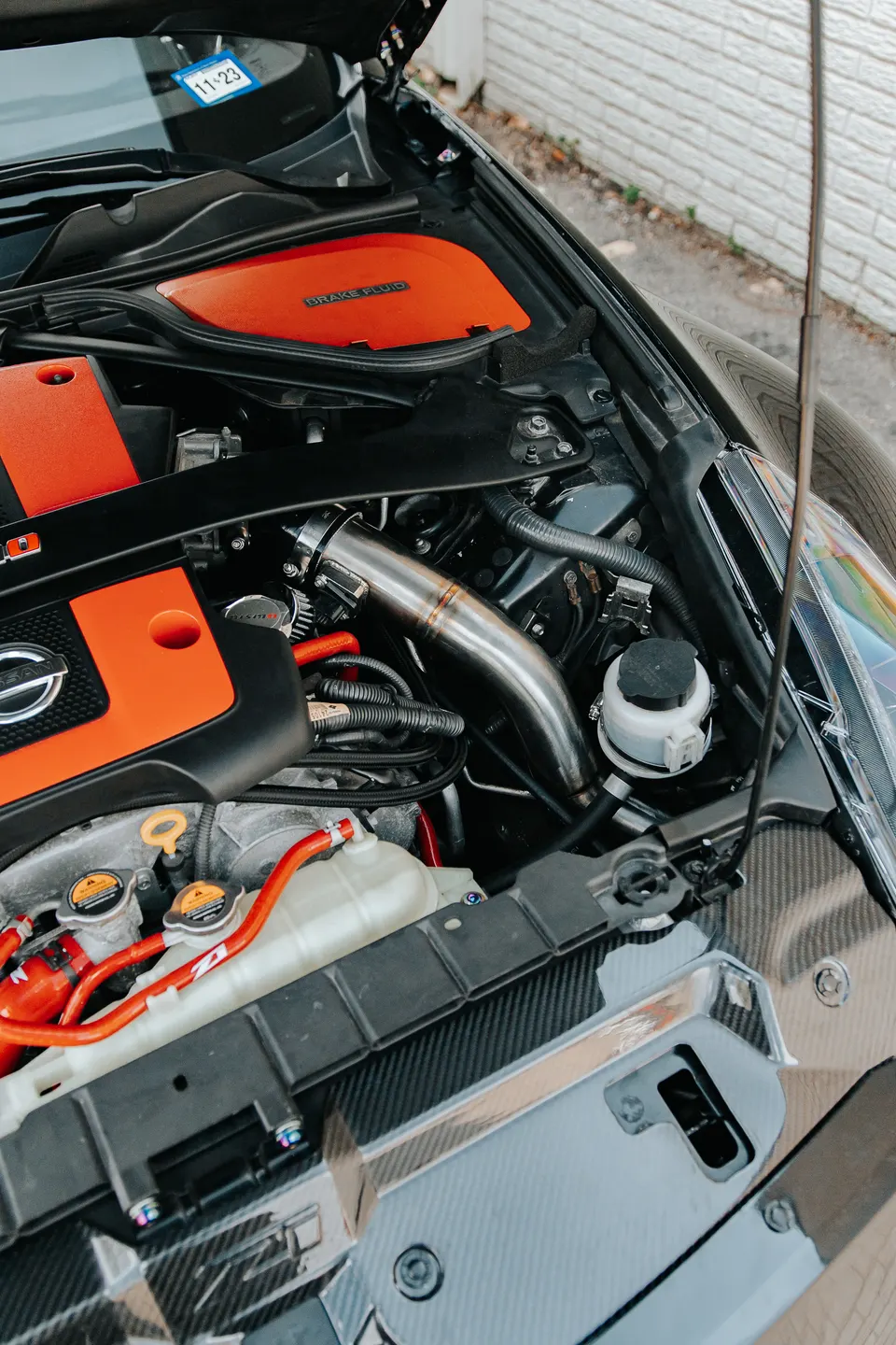 A close-up view of a modified Nissan engine bay featuring an aftermarket intake and red coolant hoses.