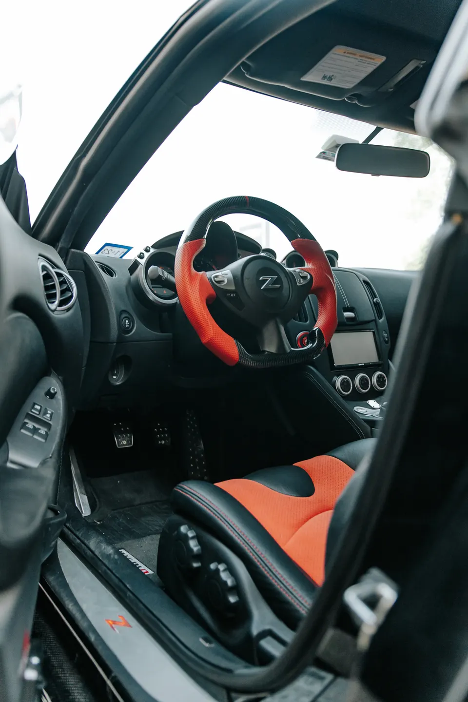 Custom red and black interior of a Nissan 370Z, featuring a carbon fiber steering wheel and sport seats.