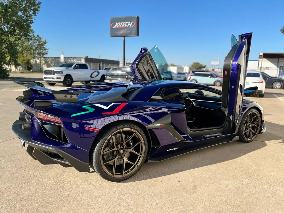 Purple Lamborghini Aventador SVJ with scissor doors open, showcasing its aggressive rear wing and custom livery at Jotech Motorsports.