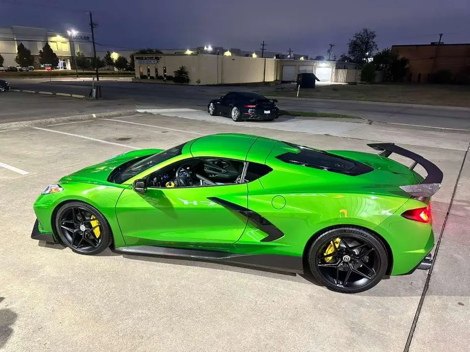 Bright green Corvette C8.R with aftermarket wheels and a large rear wing parked in a lot at night.