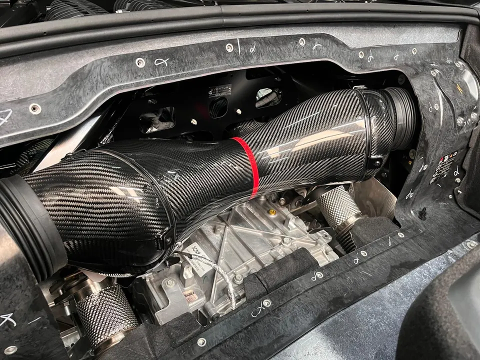 A close-up view of a carbon fiber intake system in a high-performance car's engine bay, showcasing the intricate weave.