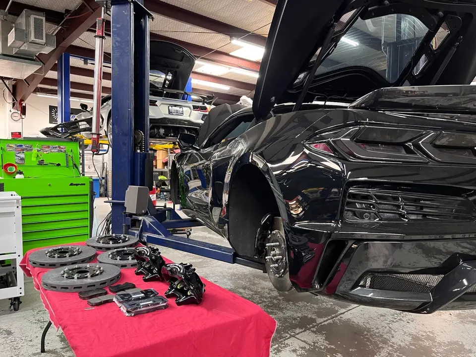 A black Corvette on a lift in a Jotech Motorsports shop, undergoing a brake system upgrade with new rotors and calipers.